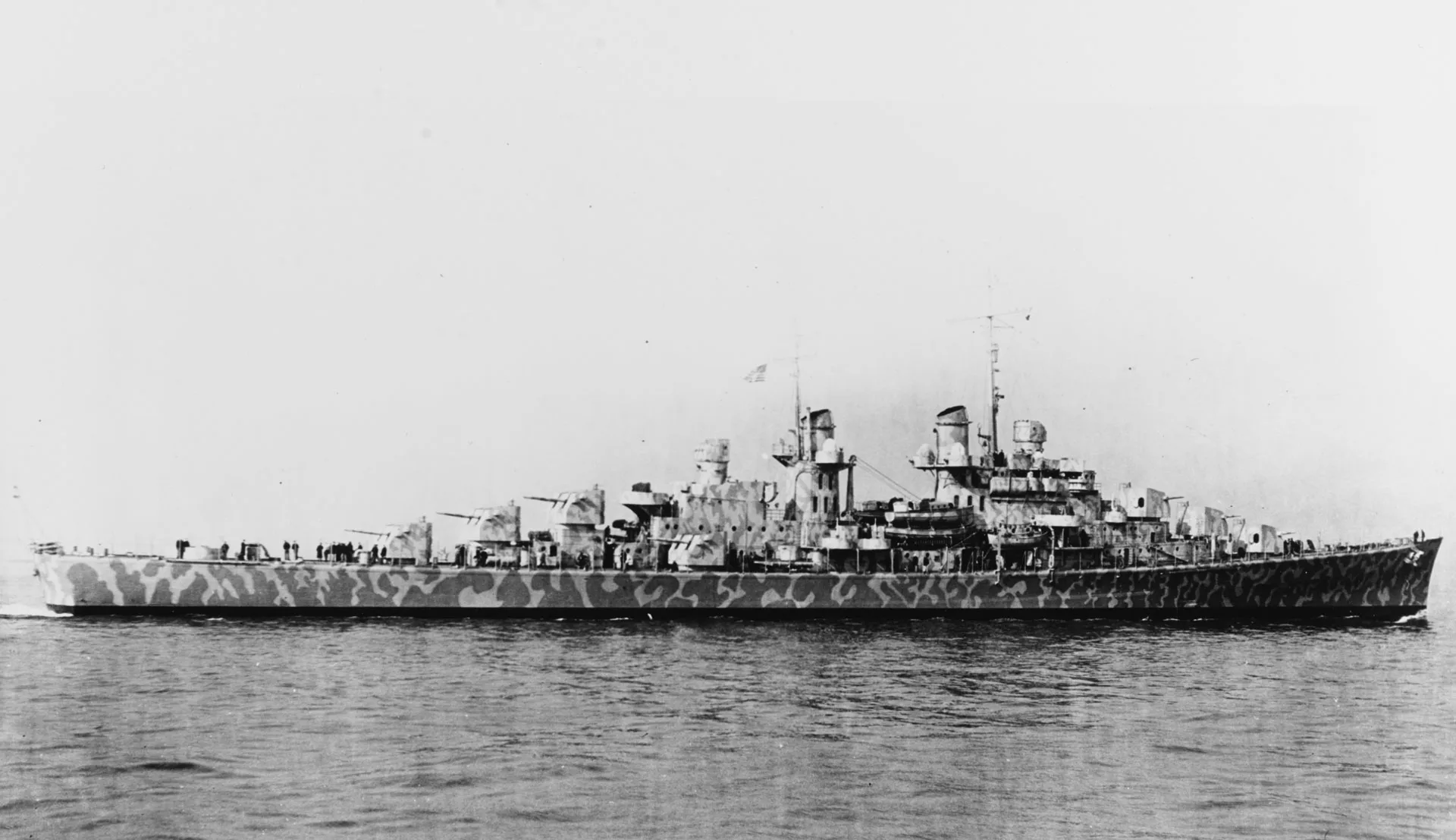 USS Juneau CL-52 underway in February 1942 wearing dazzle camouflage, crew visible along the forward deck